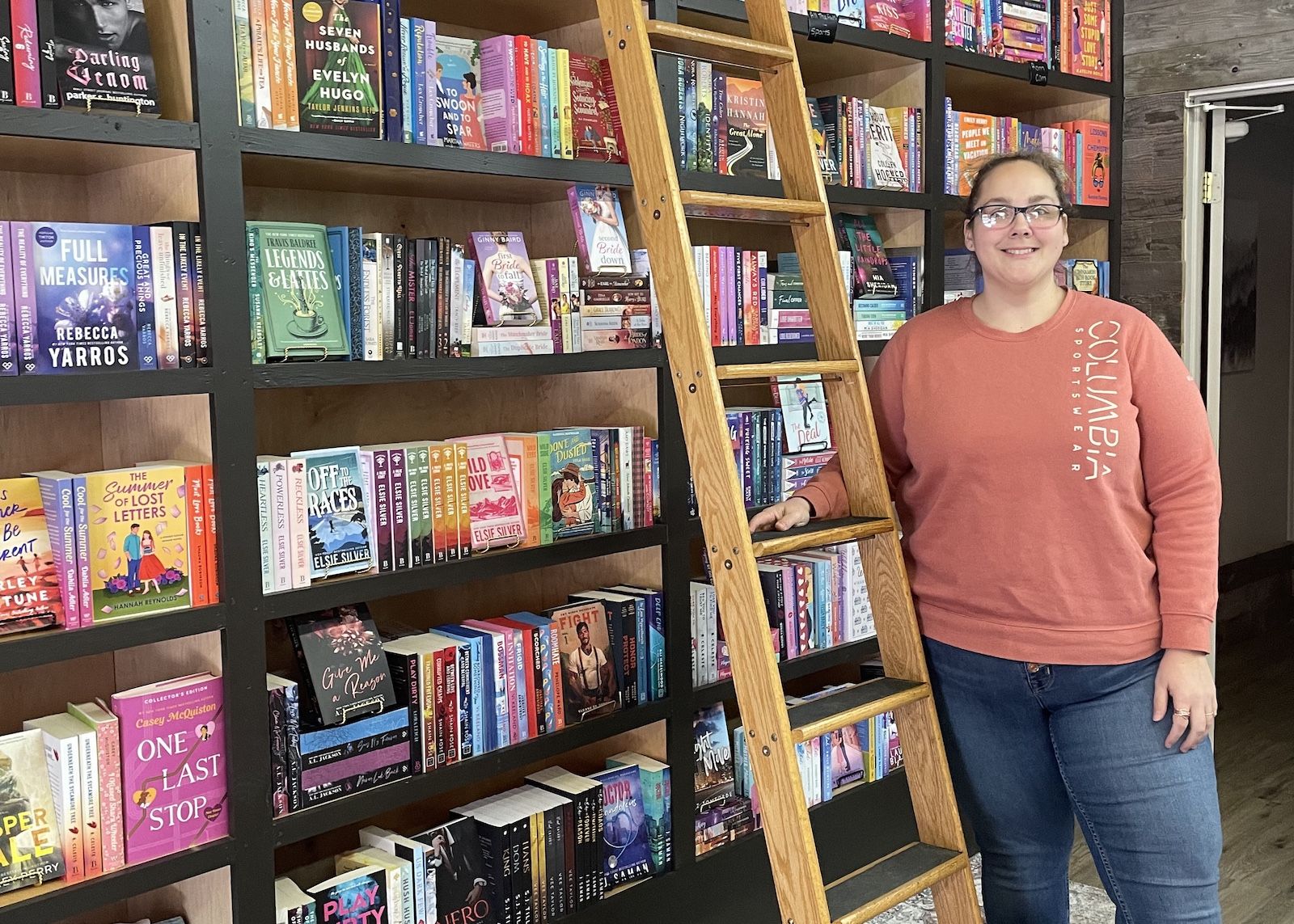 owner of just one more chapter standing in front of a ladder and many romance books