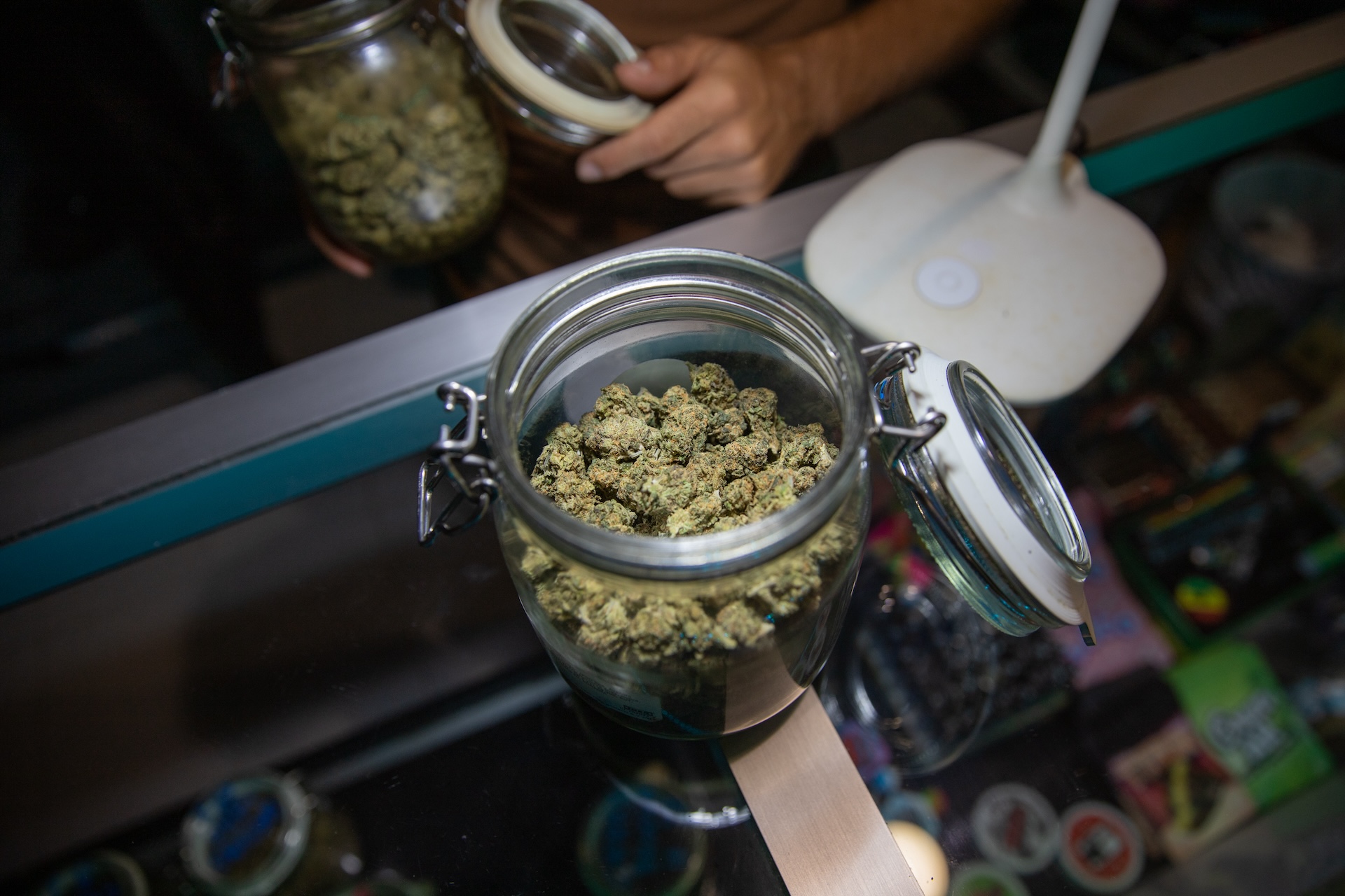A opened jar filled with raw marijuana buds on a desk inside a coffee shop.