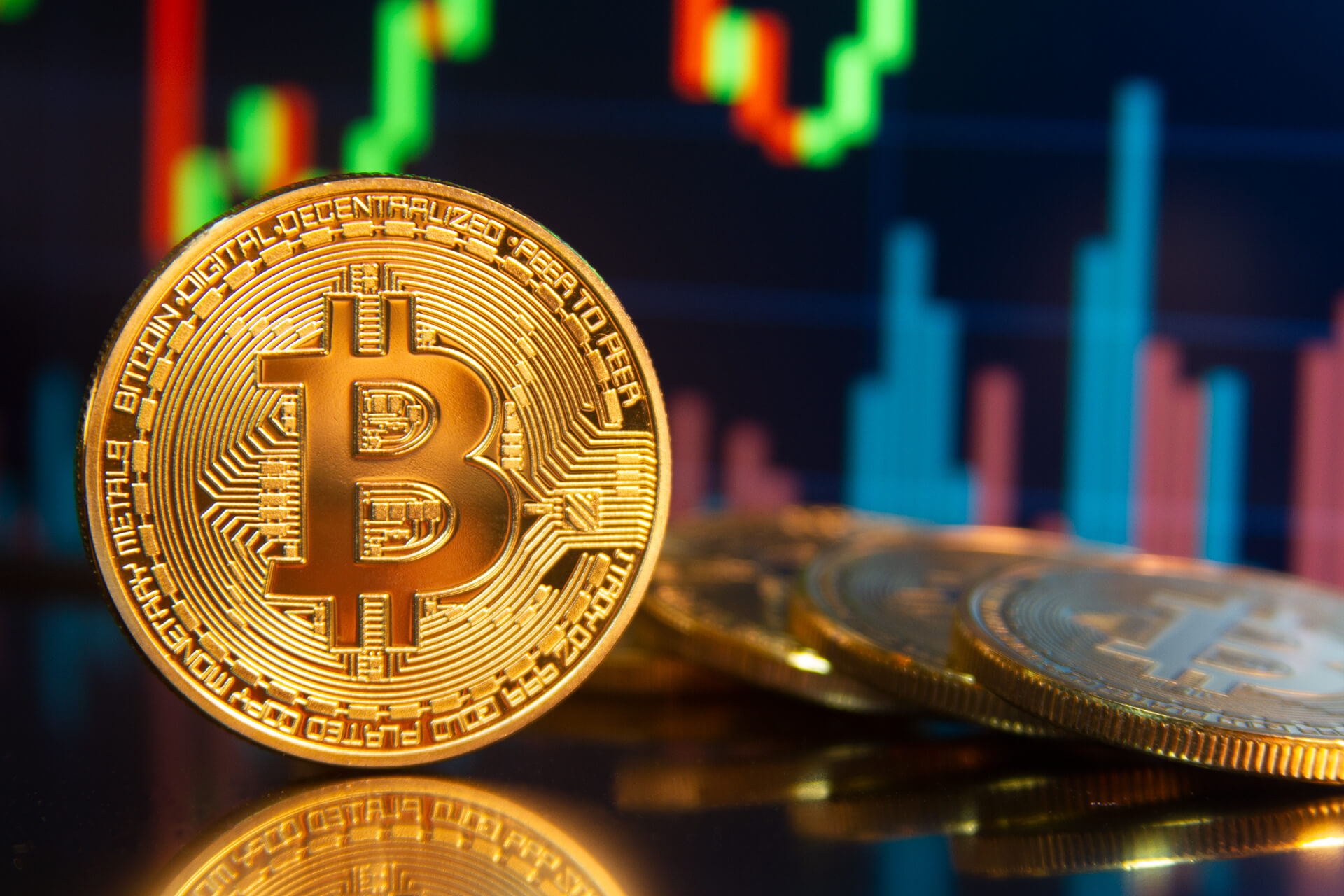 A shiny gold bitcoin infront of a pile of the same coins and a bar graph in the back