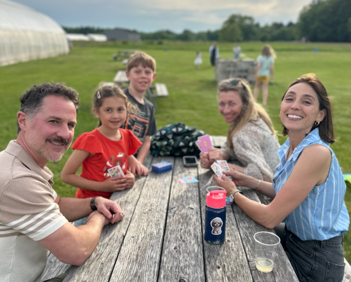 group of people at the park. two adults and three kids at picnic table.