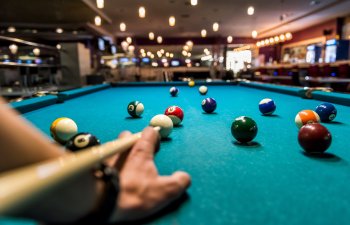 Hand with cue aiming on billiard ball at table