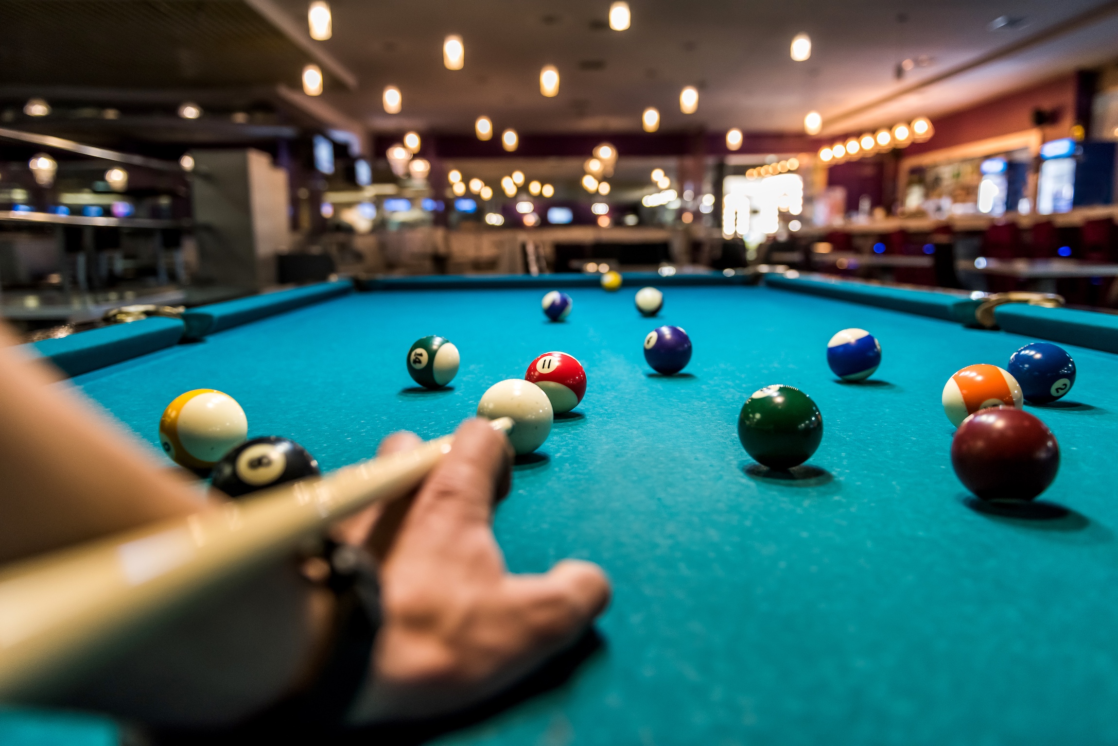 Hand with cue aiming on billiard ball at table