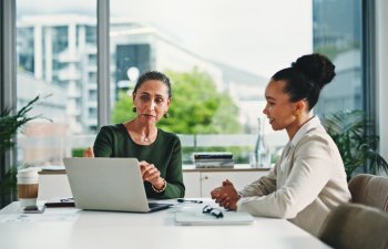 Computer, discussion and business women in office with feedback on corporate performance review. Meeting, laptop and female hr manager with employee for advice on career evaluation in workplace.