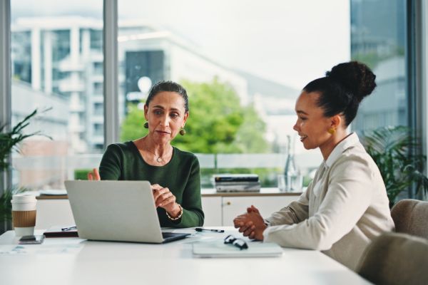 Computer, discussion and business women in office with feedback on corporate performance review. Meeting, laptop and female hr manager with employee for advice on career evaluation in workplace.